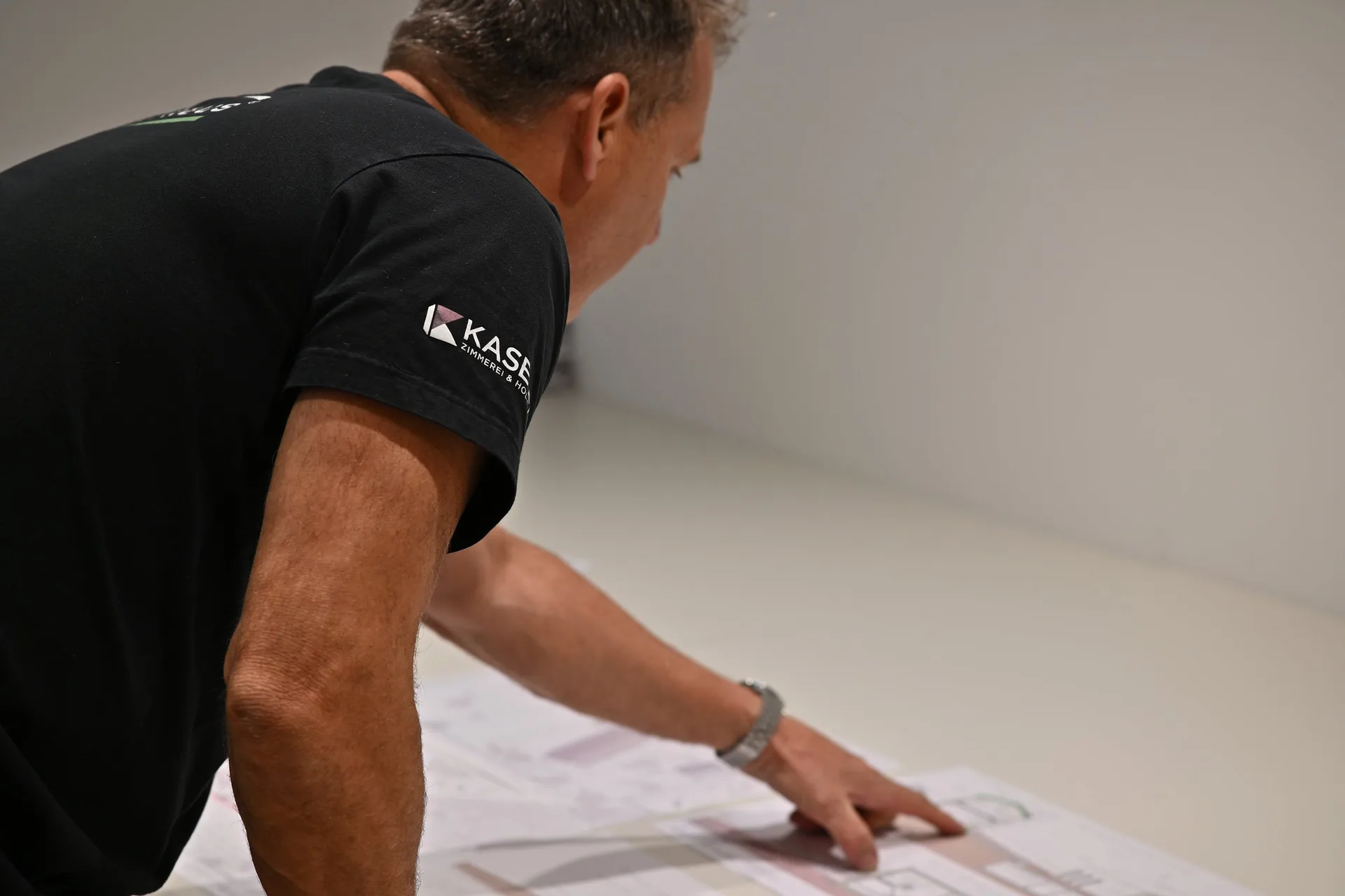 Mitarbeiter im Kaserer-Shirt beugt sich über den Tisch und zeigt auf einen Bauplan
