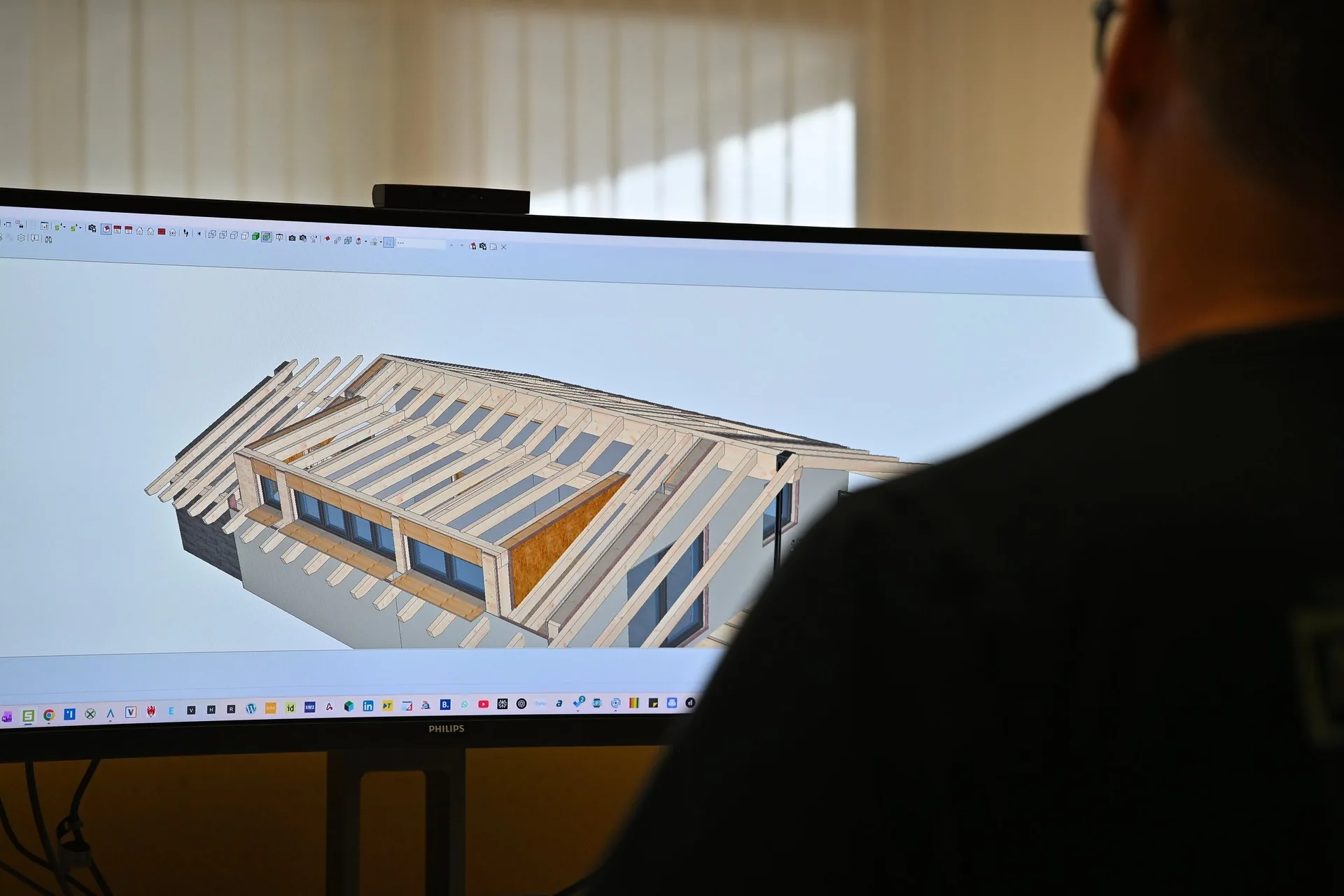 3D-Modell eines Dachstuhls auf einem breiten Monitor, davor ein Mitarbeiter