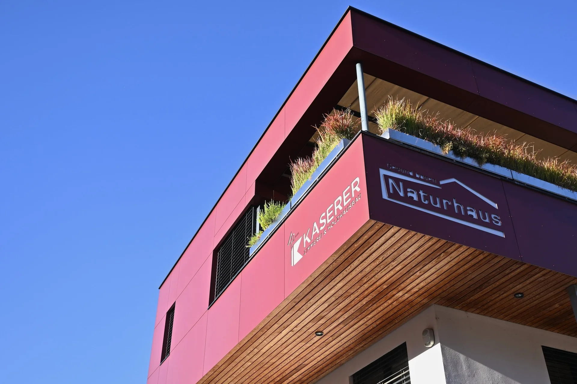 Ecke des roten Bürogebäudes von unten mit den Logos von Kaserer und Naturhaus vor blauem Himmel