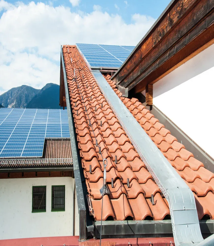 Ziegeldach mit Schneefanghaken und Sicherungsseil, dahinter Photovoltaikmodule
