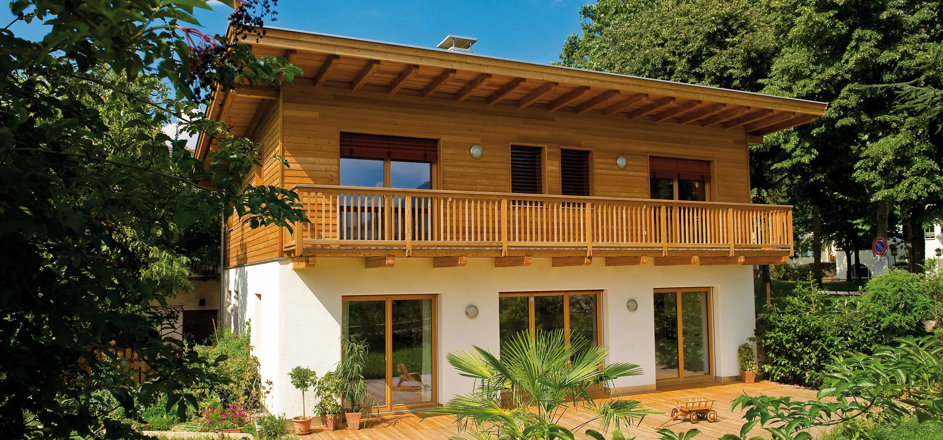 Wohnhaus mit Holzfassade im Obergeschoss, langem Balkon und Holzterrasse