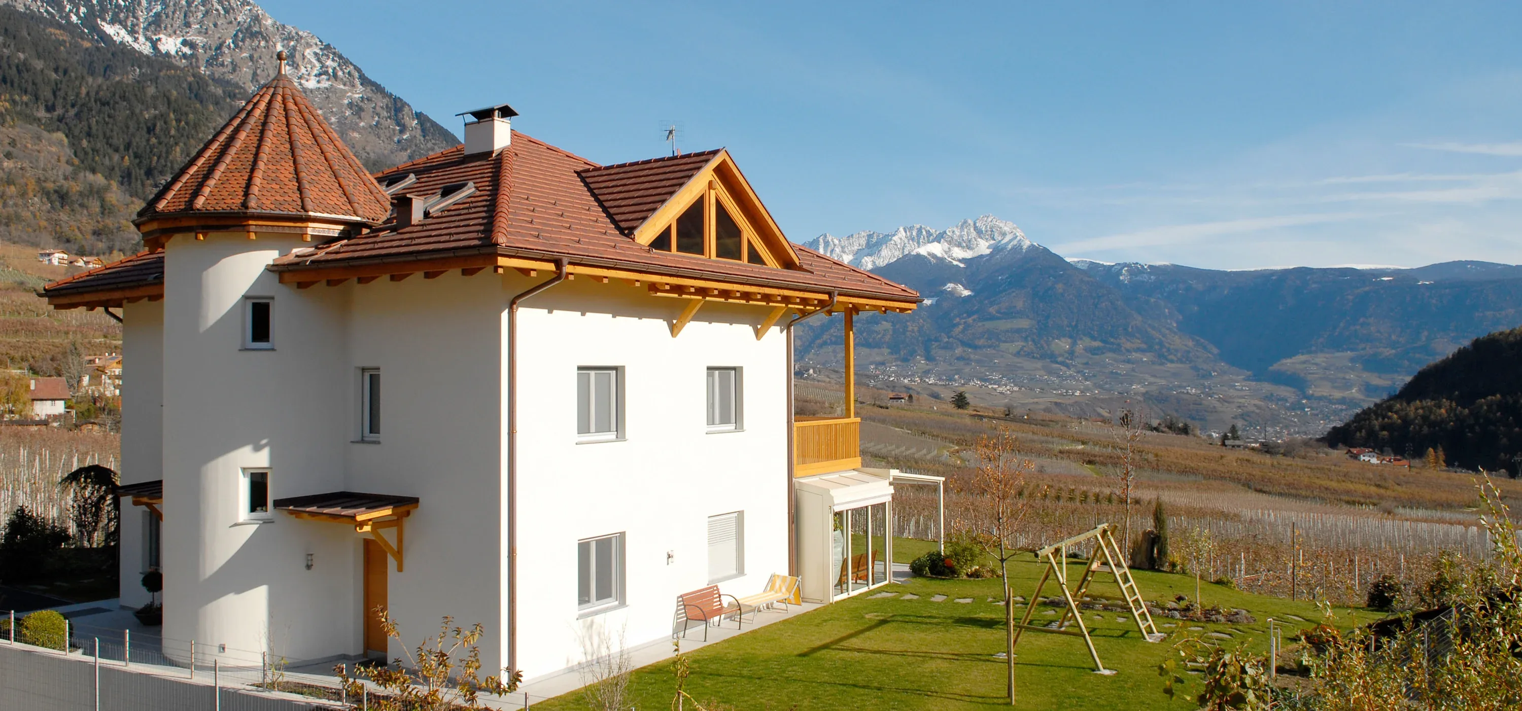Weißes Wohnhaus mit Rundturm und Ziegeldach vor verschneiten Bergen