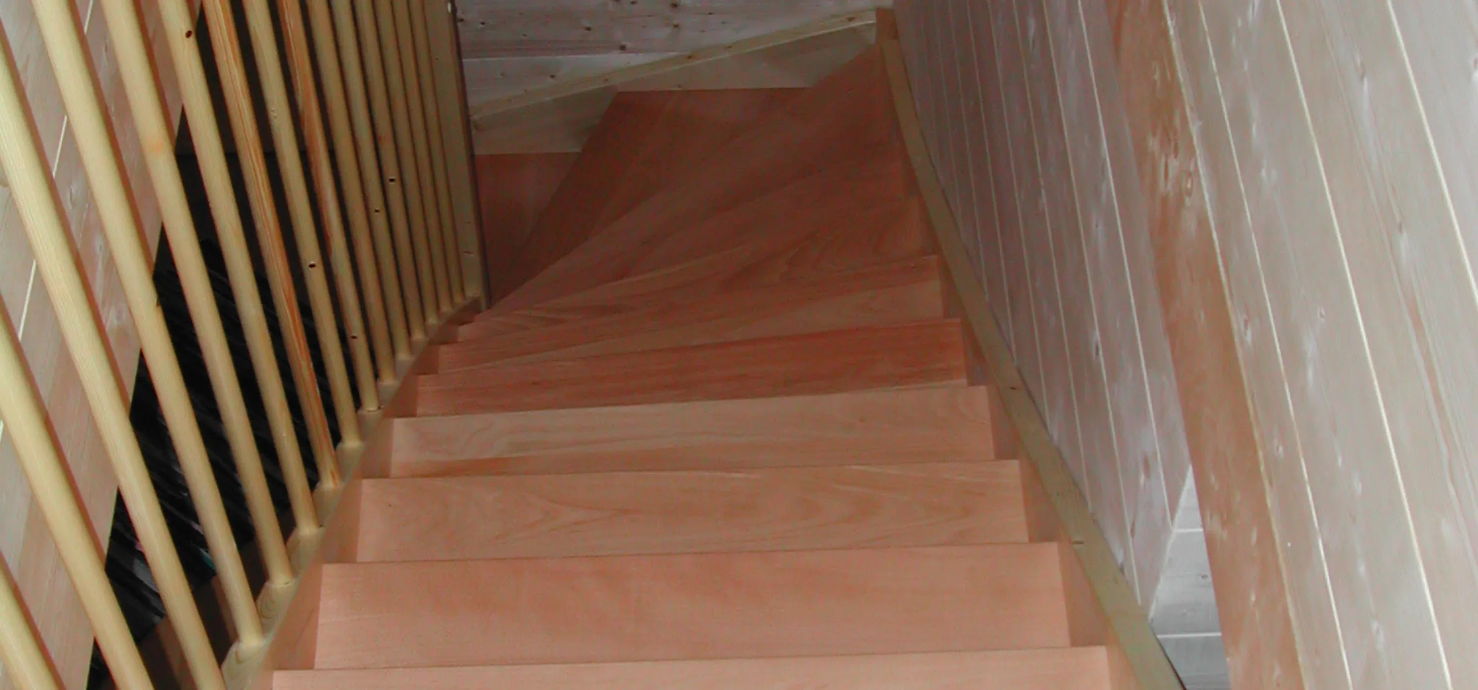 Blick von oben auf eine gewendelte Holztreppe mit Sprossengeländer