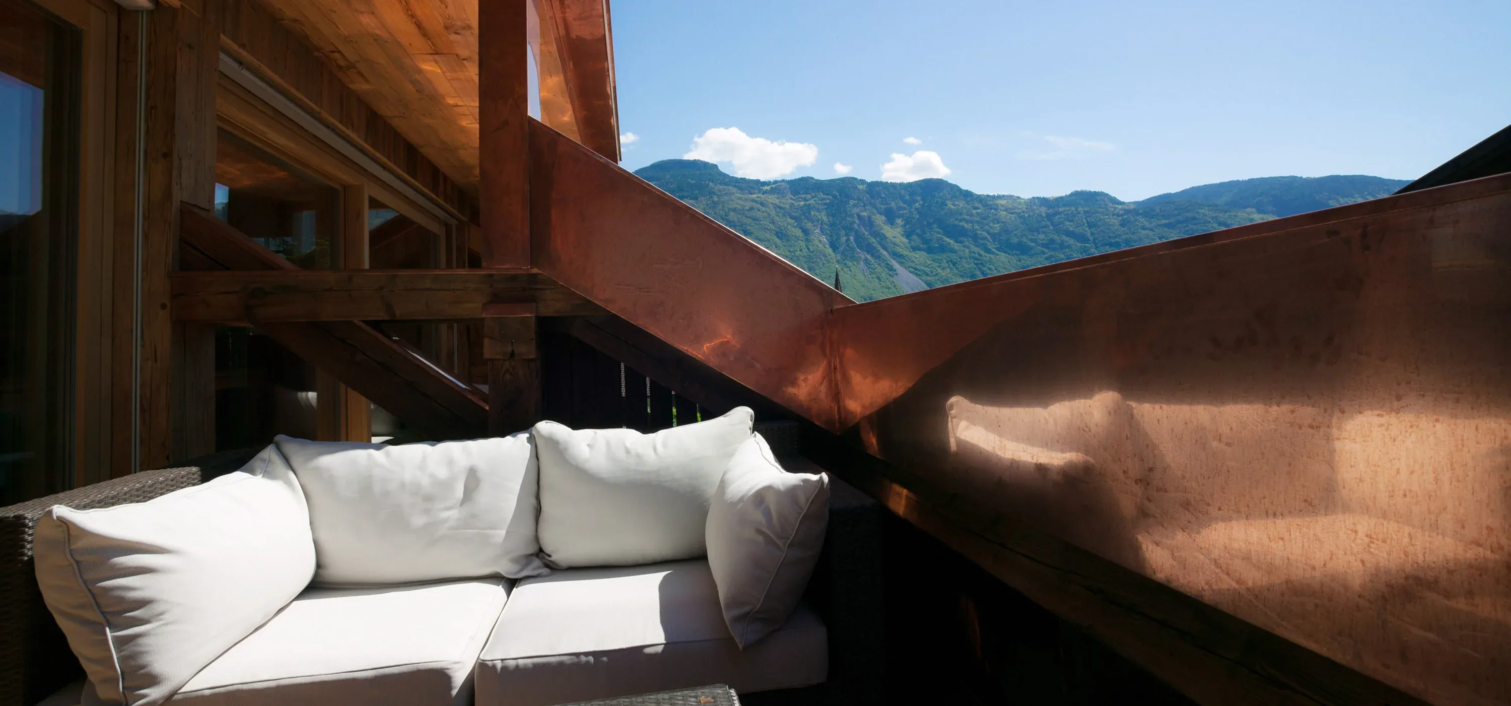 Loungesofa auf einer Holzterrasse mit Kupferbrüstung und Blick auf die Berge