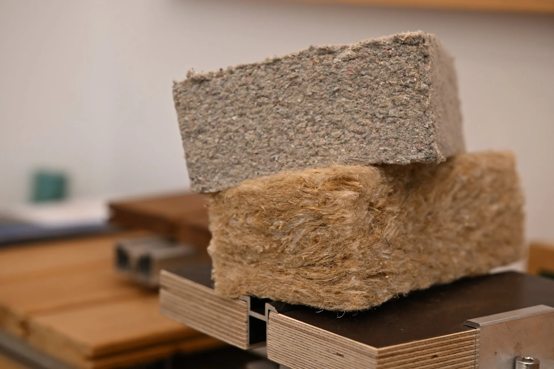 Zwei Dämmstoffmuster übereinander auf einem Holzmuster, oben grau, unten naturfarben