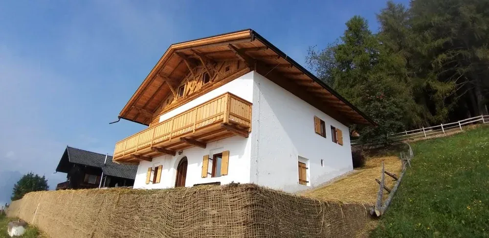 Saniertes Bauernhaus von der Seite, weiße Fassade und Balkon aus neuem Holz