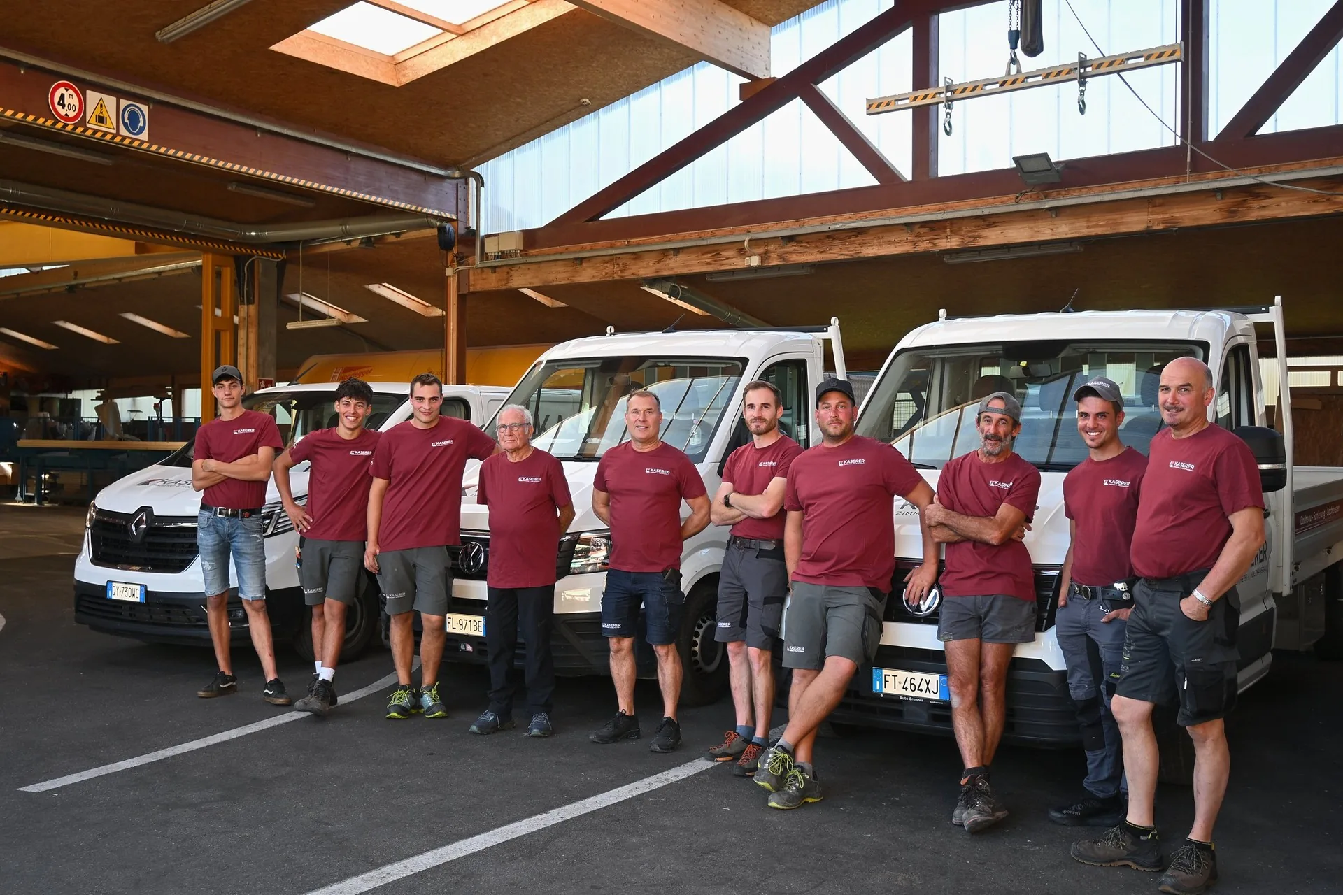 Zehn Mitarbeiter in roten Kaserer-Shirts vor den weißen Firmenfahrzeugen in der Halle