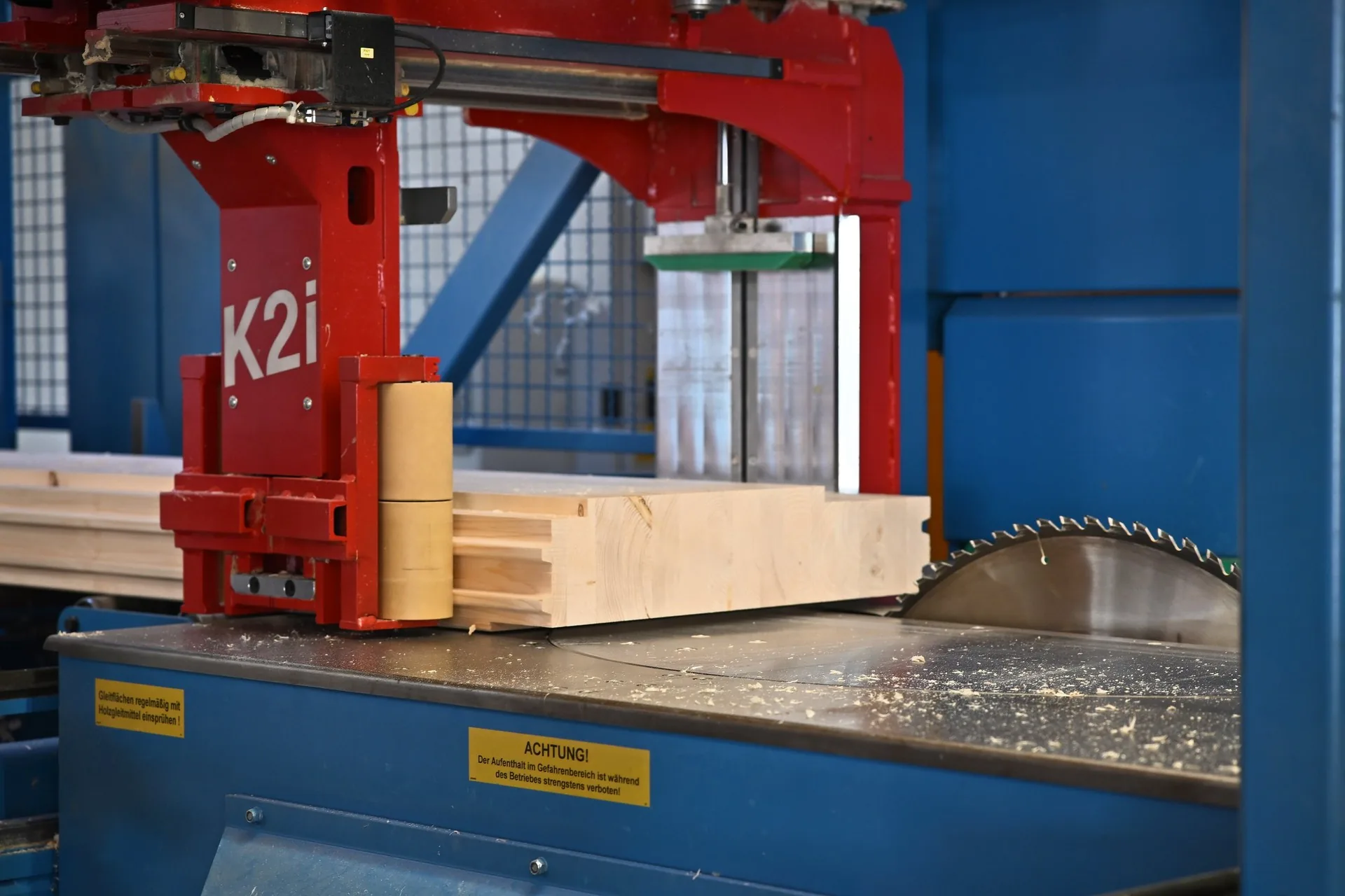 Balken an der Abbundmaschine K2i, davor das Sägeblatt und Späne auf dem Tisch