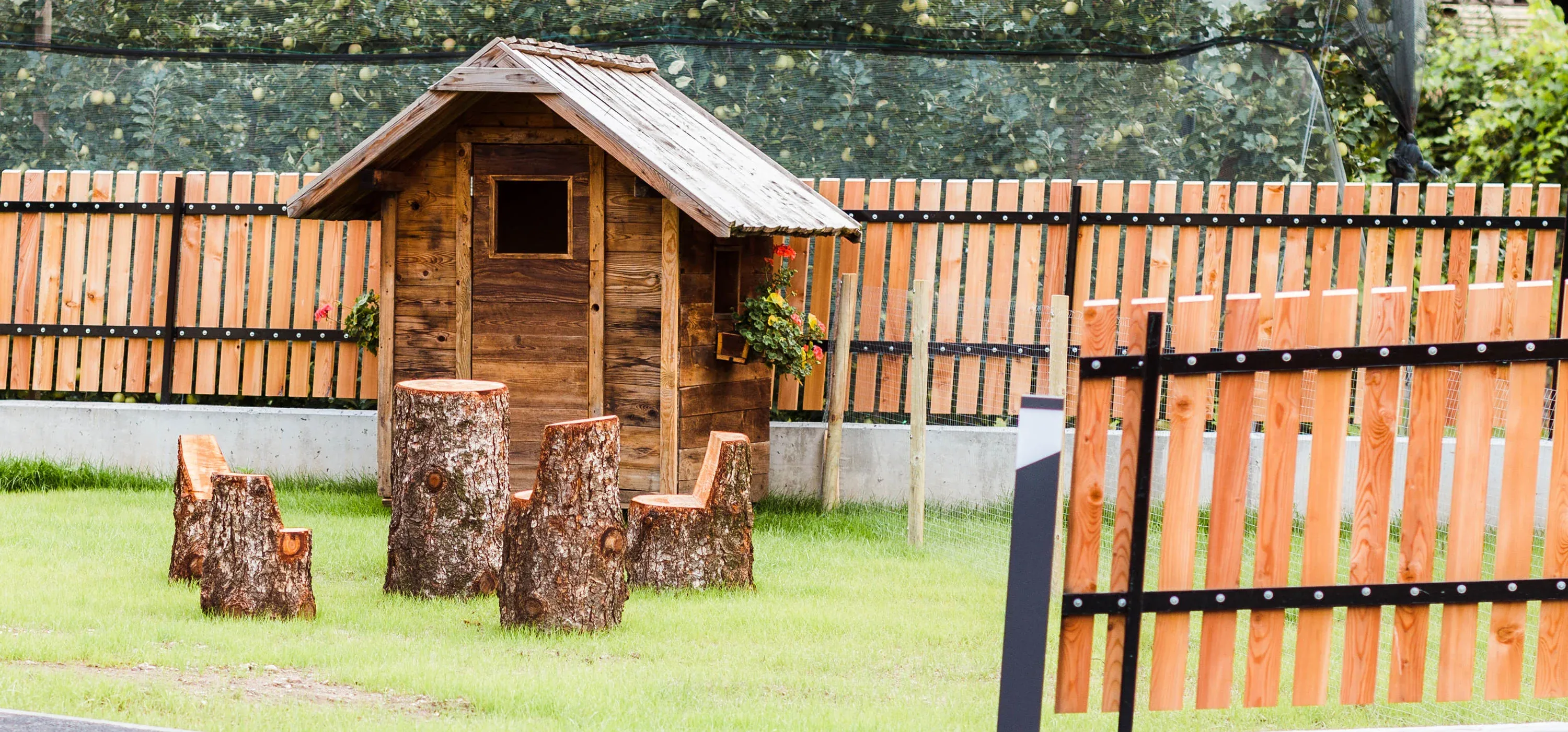 Kleines Gartenhaus aus Altholz mit Schindeldach, davor Sessel aus Baumstämmen